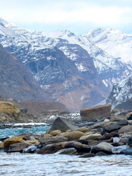 Tranquil winter view of snow-covered Himalayan mountains in Manali with rocky river.
