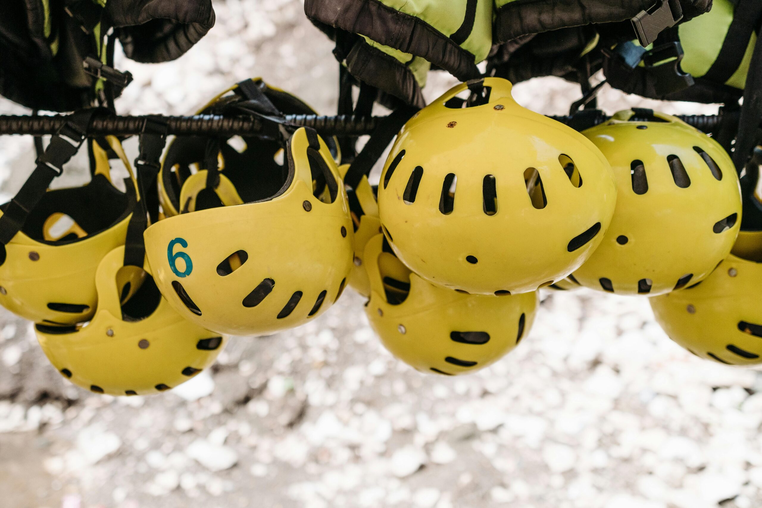 Cluster of yellow protective helmets hanging on a rack for outdoor activities like kayaking.